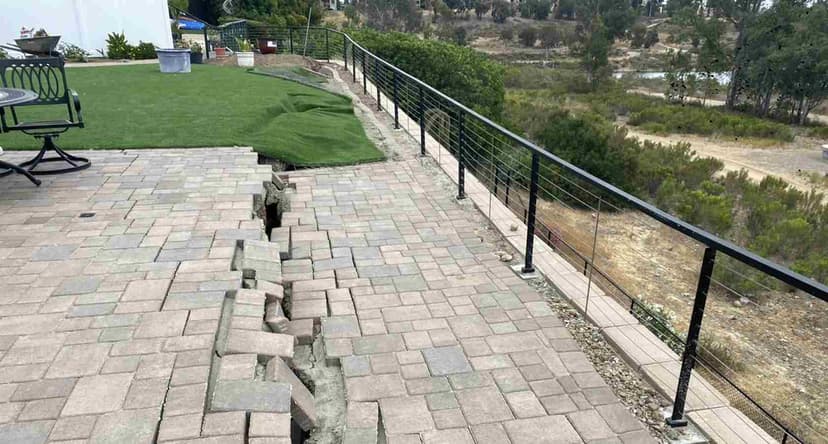 Dalinghaus Foundation Repair inspecting a retaining wall failure on a sunken patio with cracked and broken concrete.