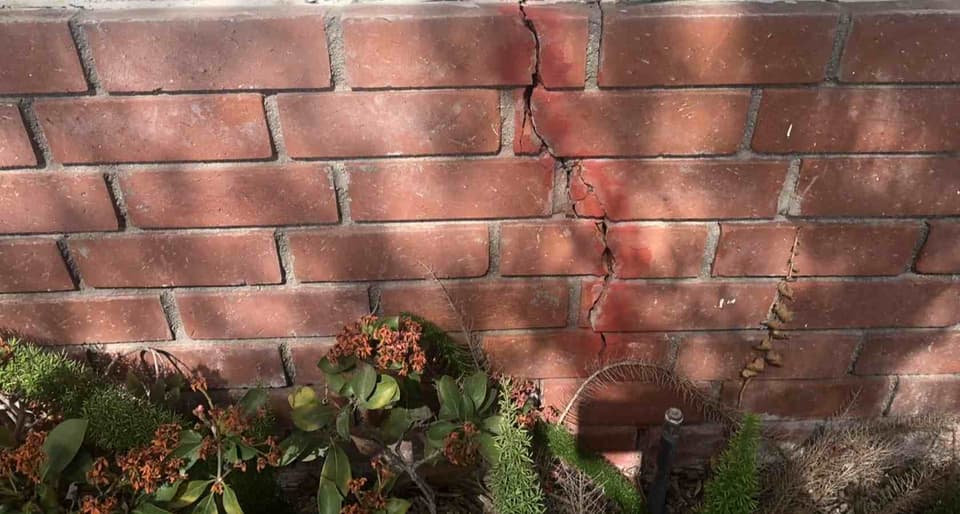 Dalinghaus Foundation Repair inspecting a vertical settlement crack in a brick retaining wall.