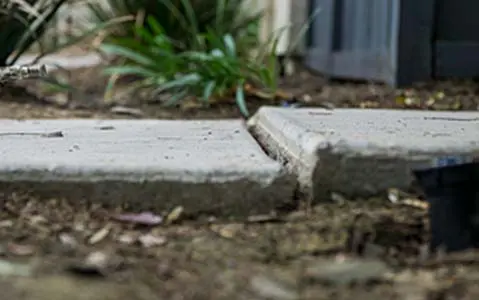 Dalinghaus Foundation Repair inspecting a concrete tripping hazard on an uneven sidewalk slab.