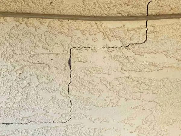 Dalinghaus Foundation Repair inspecting a stair-step crack in exterior stucco wall