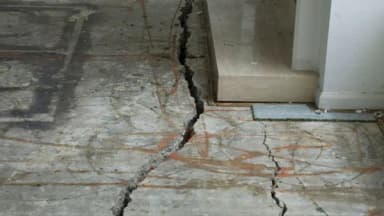 Wide cracks across a concrete slab at a doorway threshold