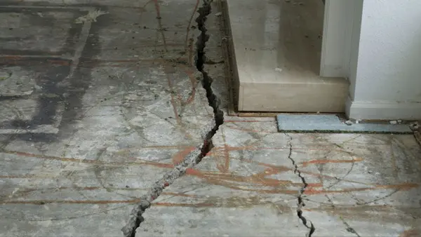 Dalinghaus Foundation Repair inspecting severe floor cracks in a concrete slab near a doorway threshold.