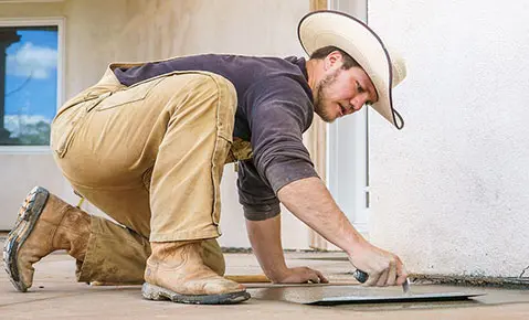 Dalinghaus Foundation Repair worker in a cowboy hat performing concrete finishing with a trowel.