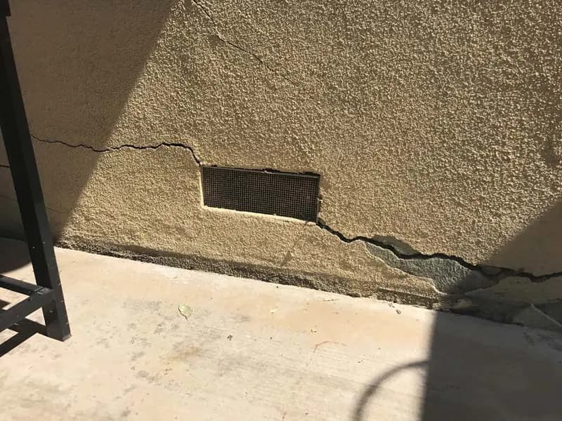 Dalinghaus Foundation Repair inspecting stucco cracking around an exterior foundation vent on a residential home.