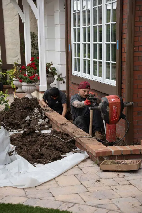 Dalinghaus Foundation Repair crew using a jackhammer during excavation for raised foundation settlement next to a paver