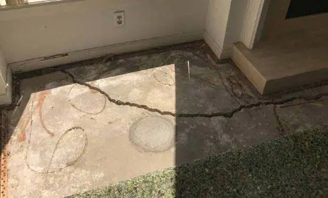 Dalinghaus Foundation Repair inspecting cracked concrete on an uneven concrete patio slab, showing structural cracking.