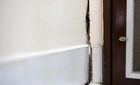 An interior wall pulling away from a door frame, leaving a wide gap and a crack