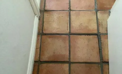 Dalinghaus Foundation Repair inspecting cracked saltillo floor tiles and grout lines near a wall, indicating foundation