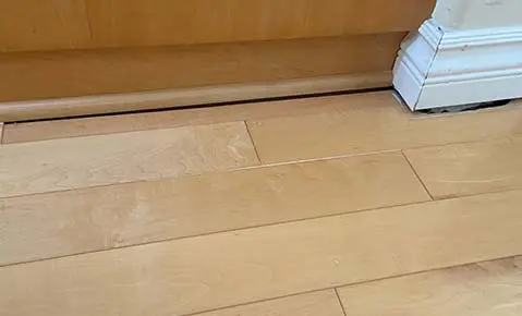 Dalinghaus Foundation Repair inspecting a gap between hardwood floor and baseboard, a sign of foundation settlement