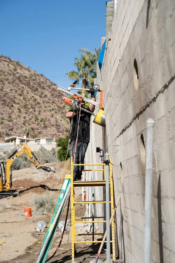 Dalinghaus Foundation Repair technician installing retaining wall tieback anchors in Tucson, Arizona with an excavator nearby
