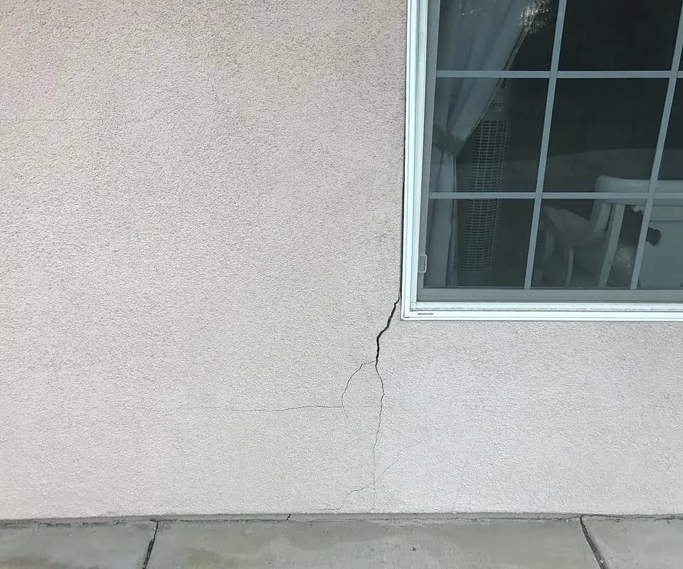 Dalinghaus Foundation Repair inspecting stucco cracking near a window corner, a common sign of foundation issues.