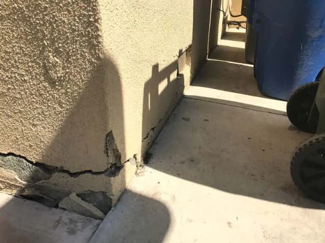 Dalinghaus Foundation Repair assessing stucco cracking on a home's foundation with damaged concrete pad.
