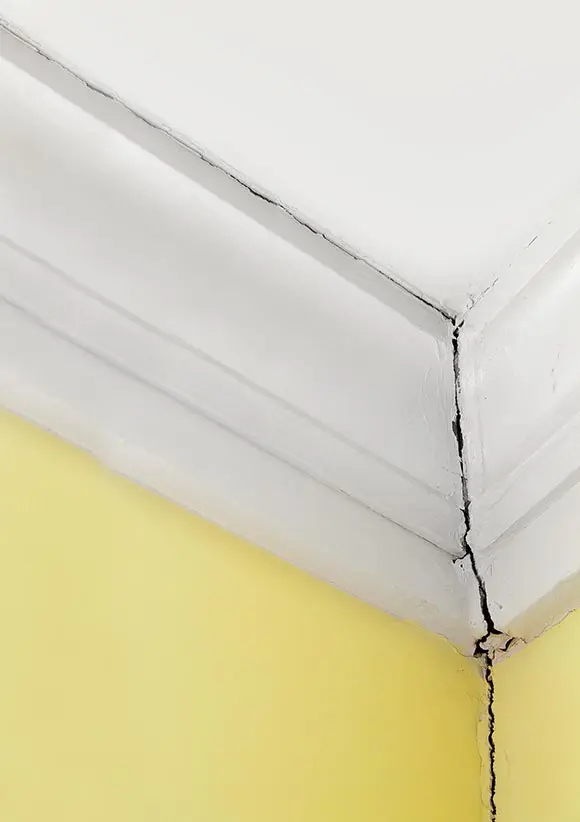Dalinghaus Foundation Repair inspecting a severe crack where a white ceiling meets a yellow wall, indicating foundation