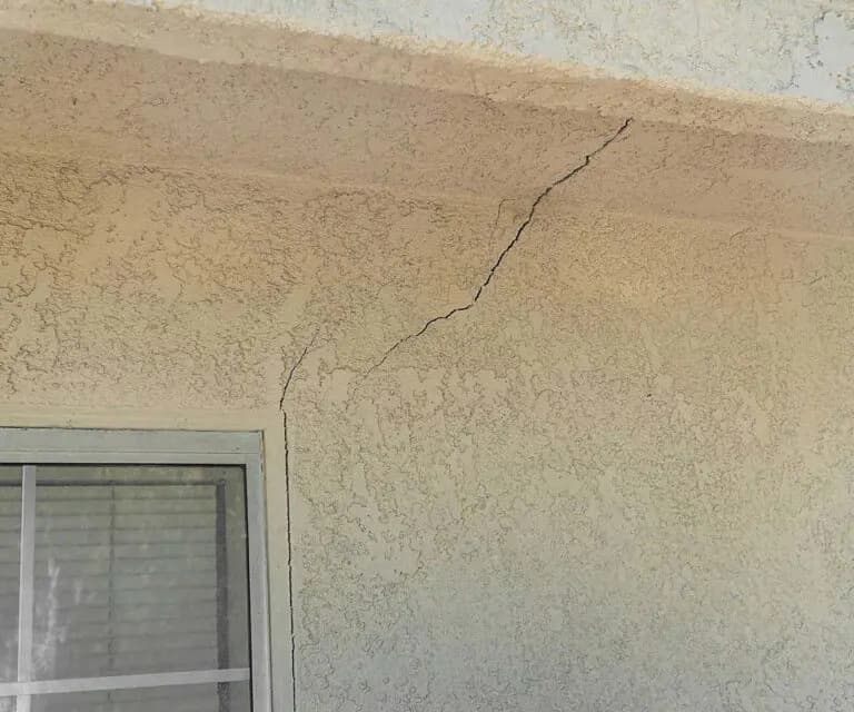Dalinghaus Foundation Repair inspecting diagonal stucco cracking above a residential window.