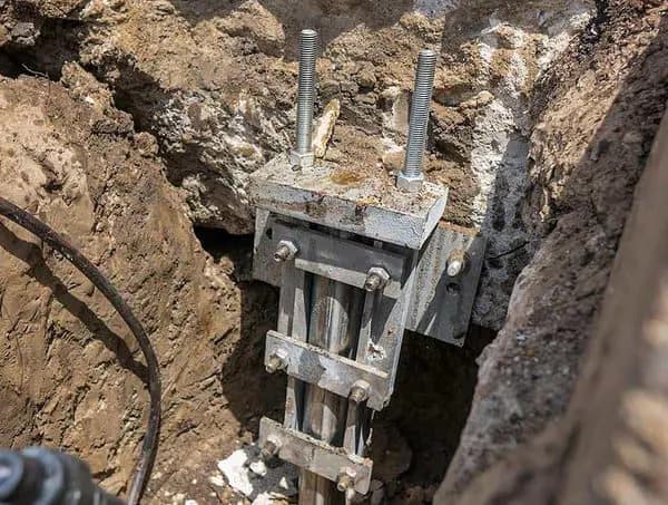 Dalinghaus Foundation Repair installing a push pier bracket bolted to a concrete footing in an excavated trench.