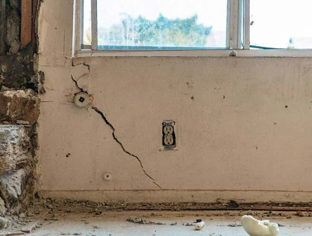 Dalinghaus Foundation Repair inspecting severe diagonal cracks in an interior drywall wall beneath a window.