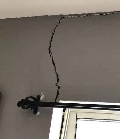 A long crack running up an interior wall from the top of a window frame