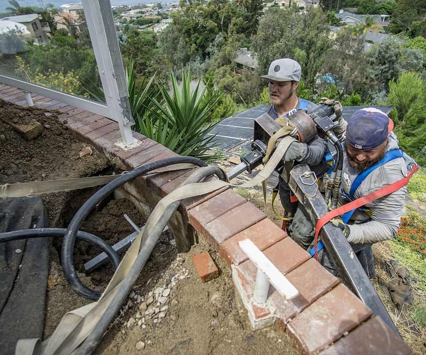 Dalinghaus Foundation Repair crew installing helical tieback anchors for a retaining wall, using a rotary drive head.