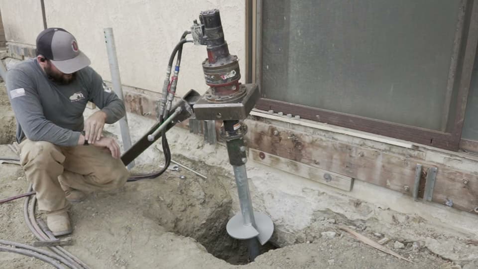 Dalinghaus Foundation Repair crew installing a helical pier with a rotary drive head for foundation underpinning.