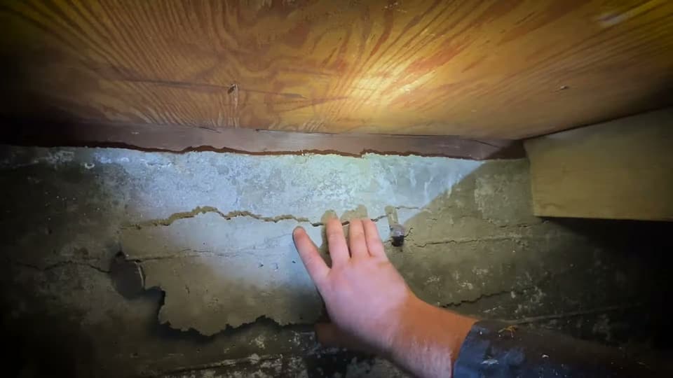 Dalinghaus Foundation Repair expert inspecting concrete spalling and cracking in a crawl space foundation wall.