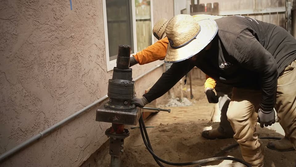 Dalinghaus Foundation Repair crew installing helical tieback anchors with a rotary drive head for foundation stabilization.
