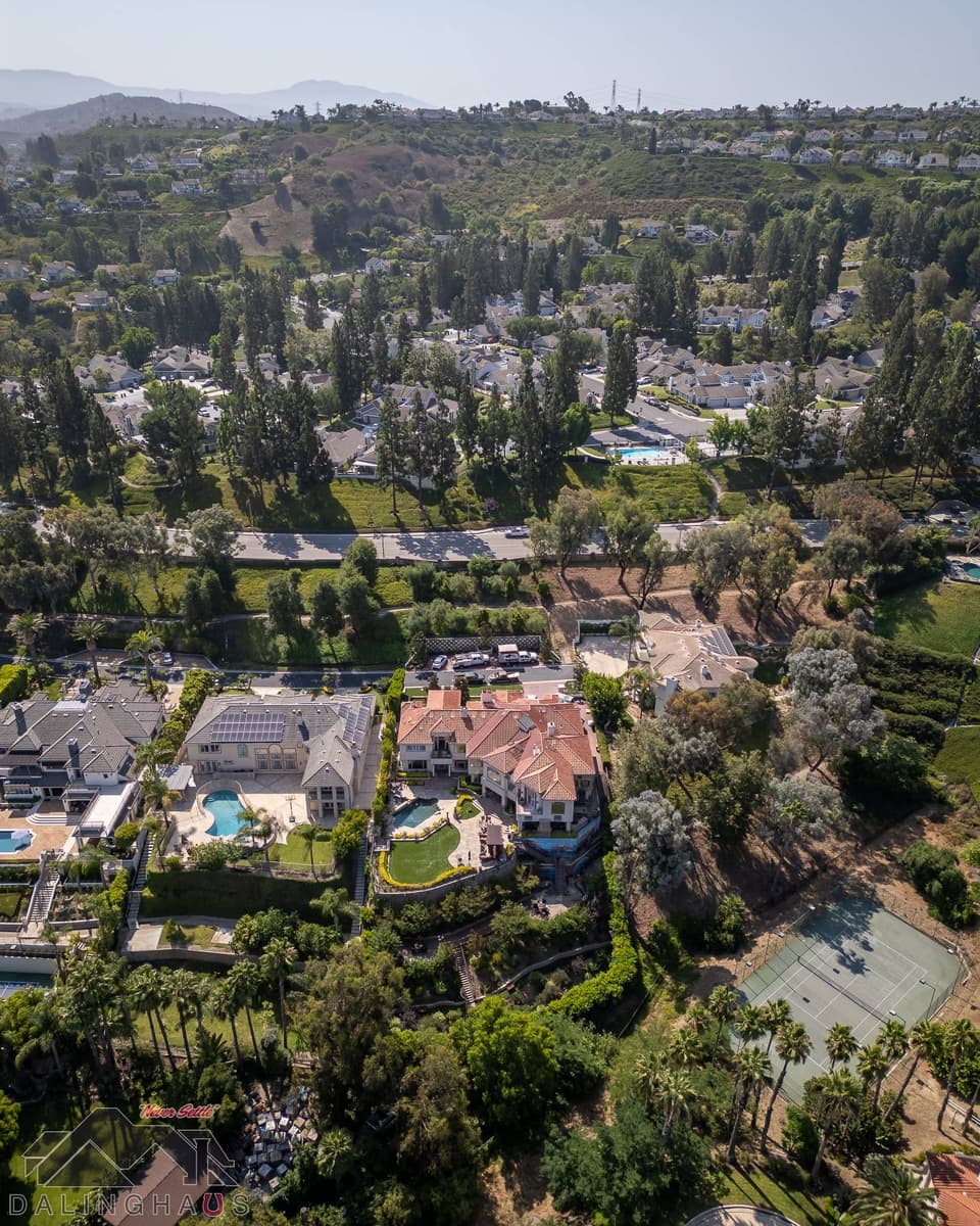 Aerial view of a tiled roof Anaheim home above a canyon road, with tract homes and hills beyond.