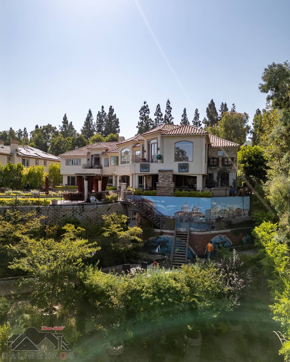Rear elevation seen from the slope below, with mural covered retaining walls and a staircase beneath the house.