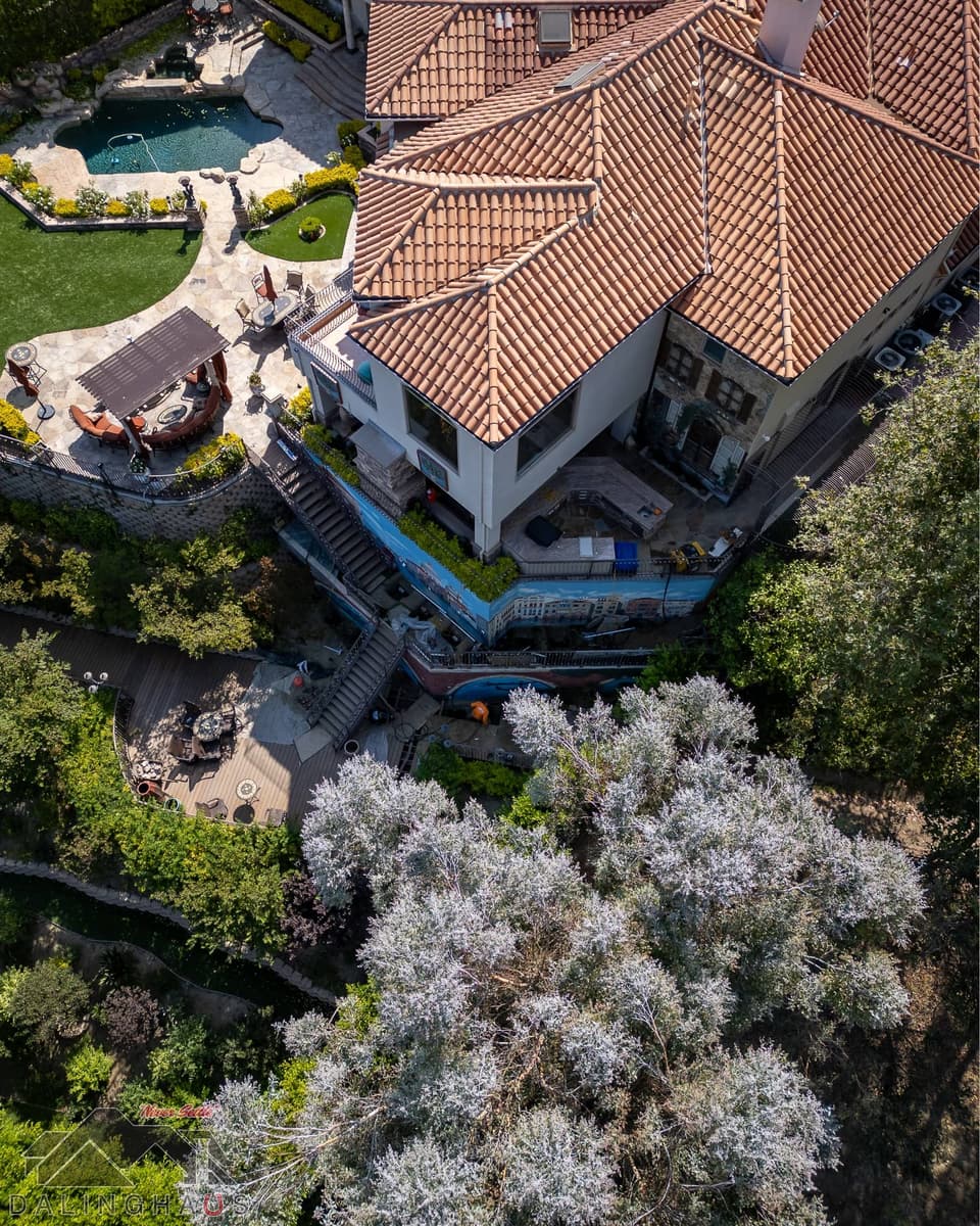 High angle over the roof corner showing the pergola, pool and mural walls stepping down the hill.
