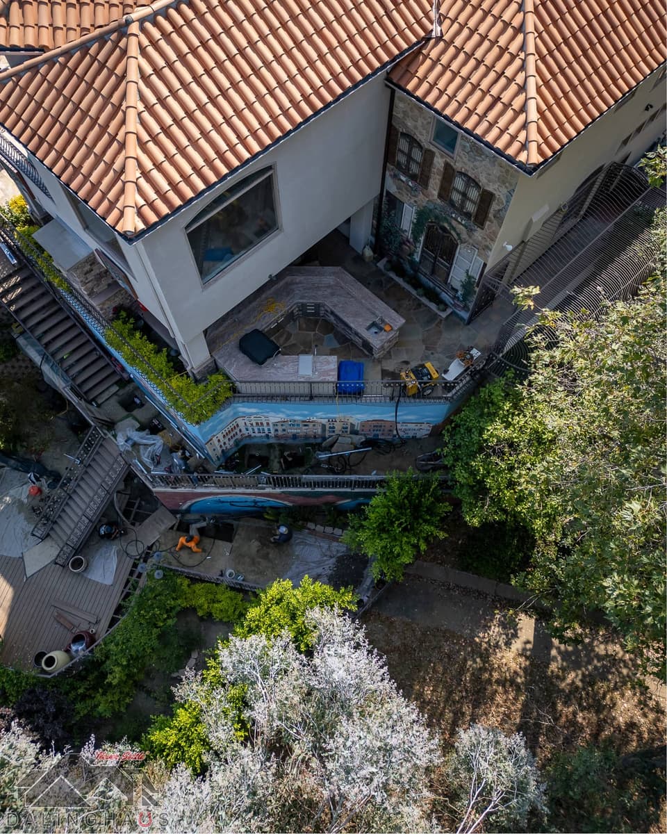 Nearly vertical drone shot of the roof corner, terrace and an open excavation along the base of the painted wall.