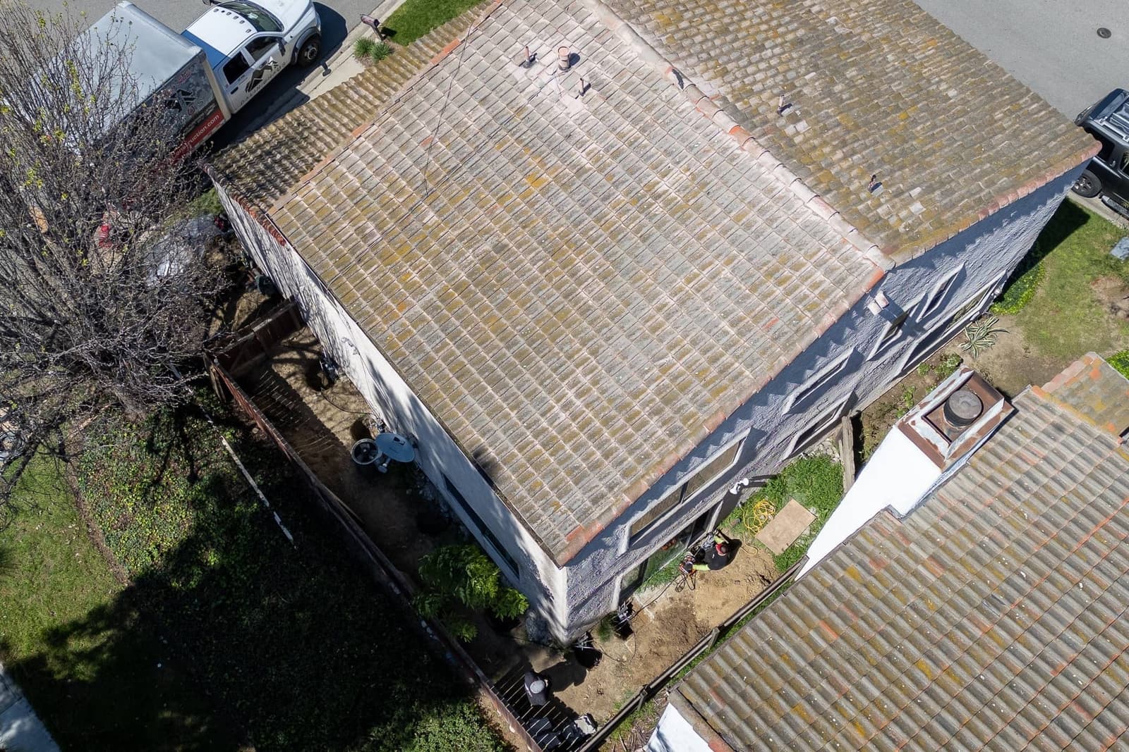 Drone view straight down over the tile roof, crew truck at the curb and workers in the side yard