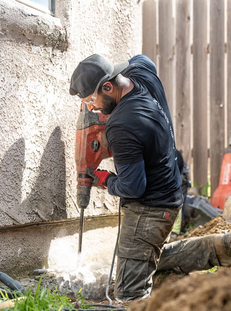 Worker in safety glasses breaking the footing with a red rotary hammer as concrete dust rises