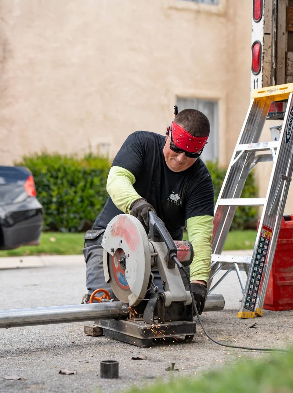 Worker cutting a steel pier pipe on a chop saw in the driveway, sparks flying