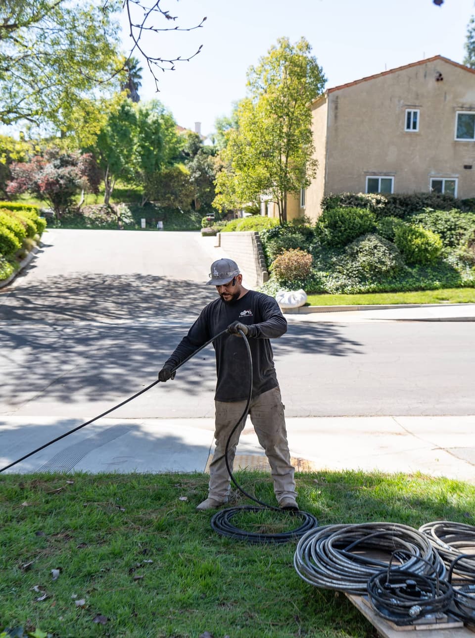Crew member uncoiling black hydraulic hose across the front lawn with more coils stacked on a pallet