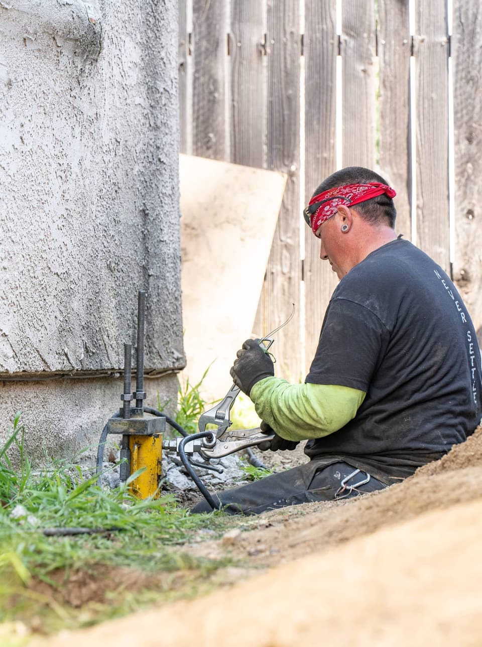 Worker with locking pliers tightening a hydraulic fitting on the yellow lift ram at the footing