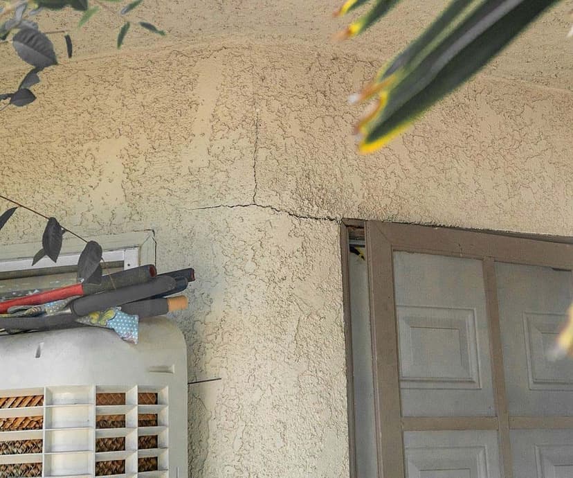 A crack in exterior stucco running sideways from the top corner of a door frame