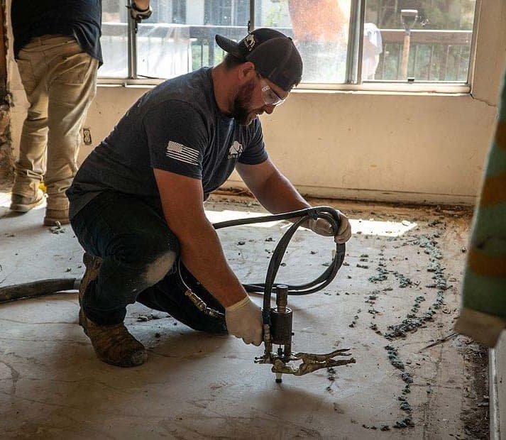 Crouching worker in safety glasses and gloves injecting foam through a port in the interior slab