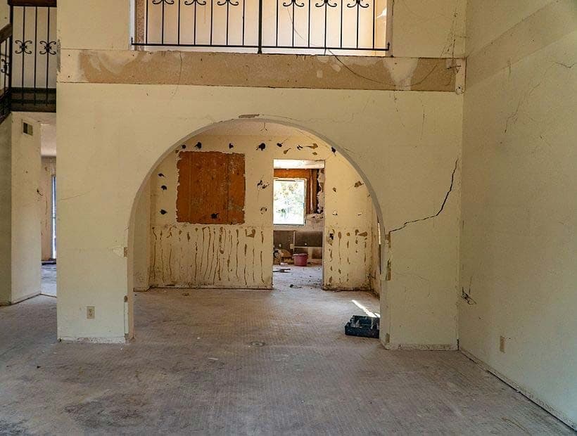 Gutted living room with an arched opening, cracks in the plaster above the arch and along the right wall