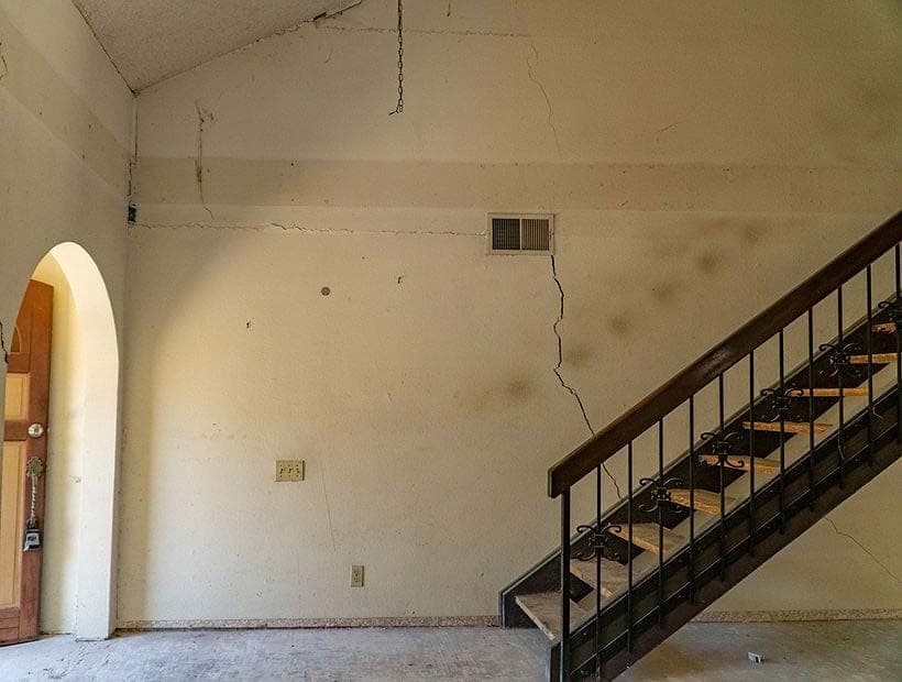 Bare interior wall beside an iron railed staircase with a long diagonal crack running down from the vent