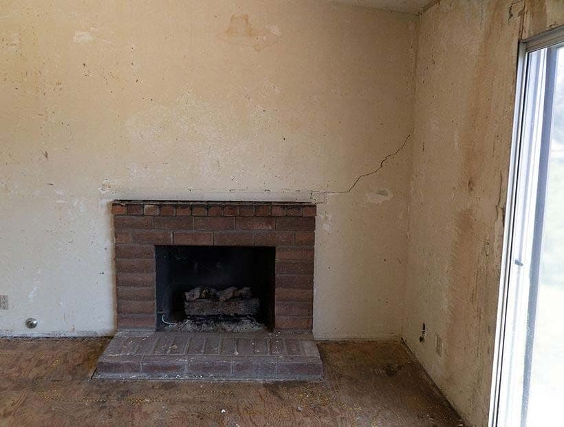Brick fireplace on a stripped wall, a crack running up and to the right from the top of the mantel