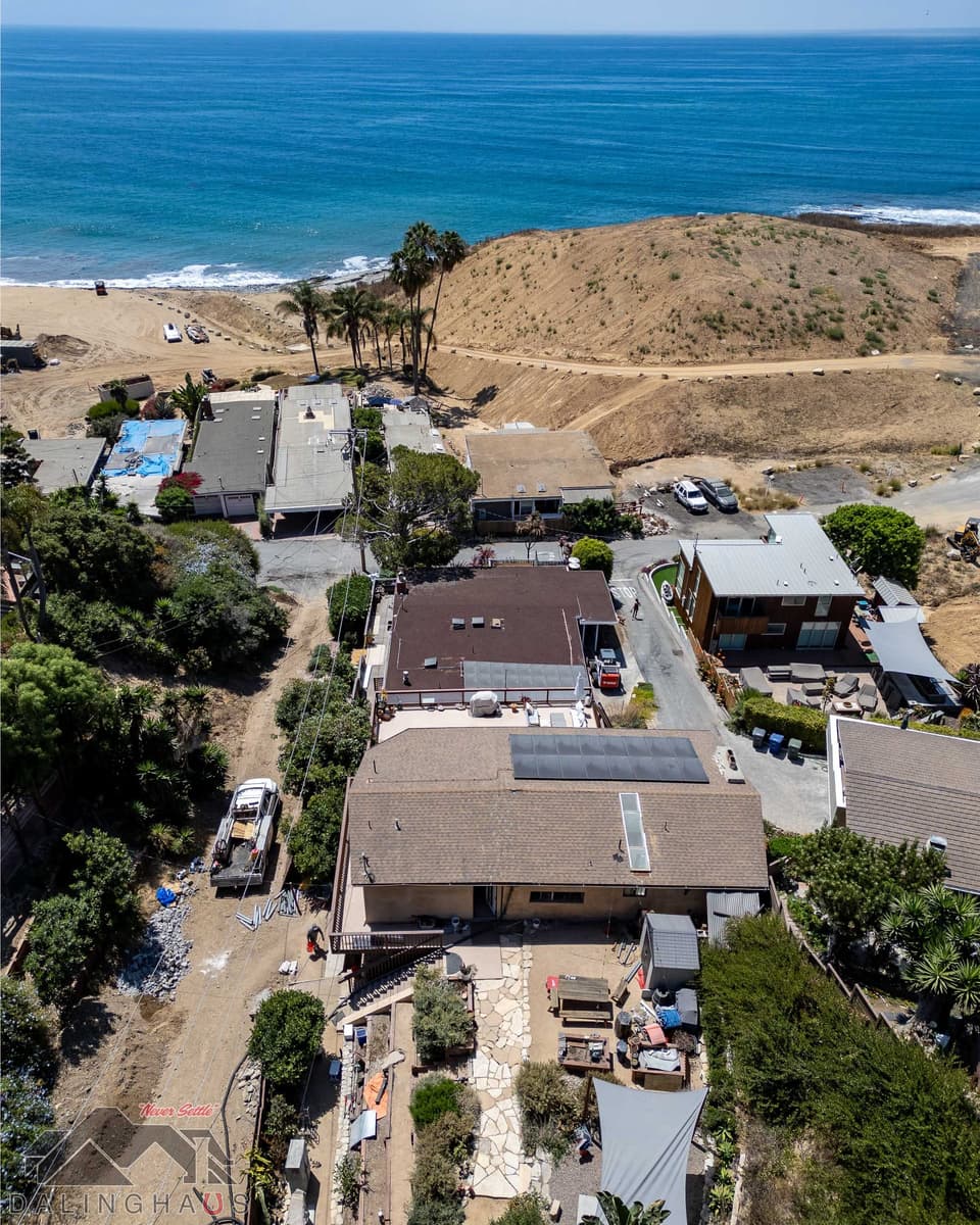 Aerial of the two story stucco home beside the beach, a crew truck unloading steel pier sections at the driveway