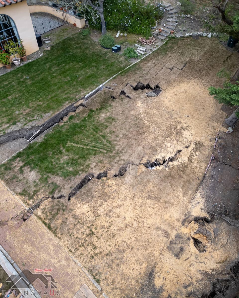 Overhead view of a lawn torn by zigzag fissures with a brick path and a fallen tree stump