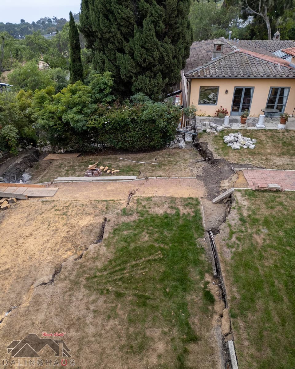 Cracks stepping across a lawn and a brick walkway toward the single story wing of the home