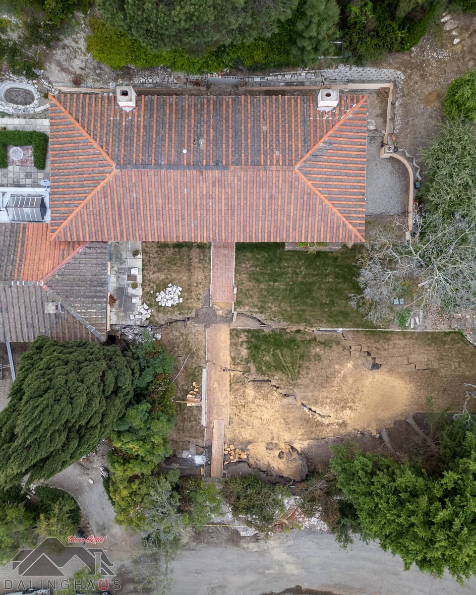 Straight down aerial of a tile roof, cracked lawn and lumber stacked along a brick path