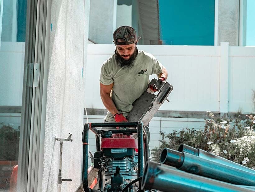 Bearded crew member in a green shirt carrying a steel push pier bracket over a gasoline hydraulic power unit