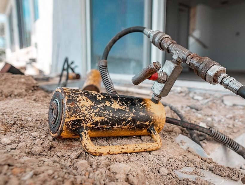 Scuffed yellow hydraulic ram with a control valve resting on loose dirt near a sliding door