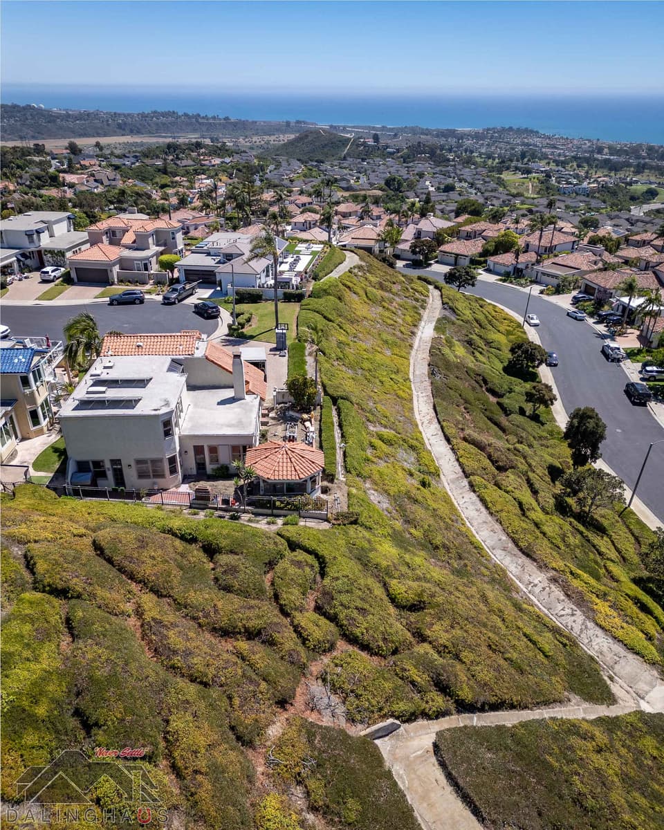 Drone view of a two story stucco home with a tile roof on a hillside ridge above the ocean