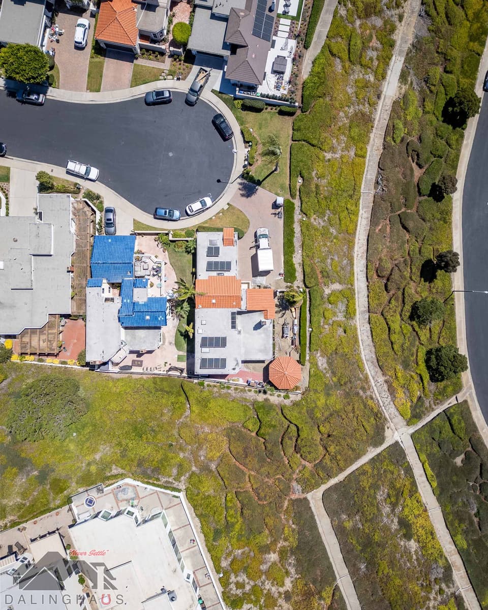 Straight down aerial of the house and neighboring roofs with a concrete drainage channel crossing the slope