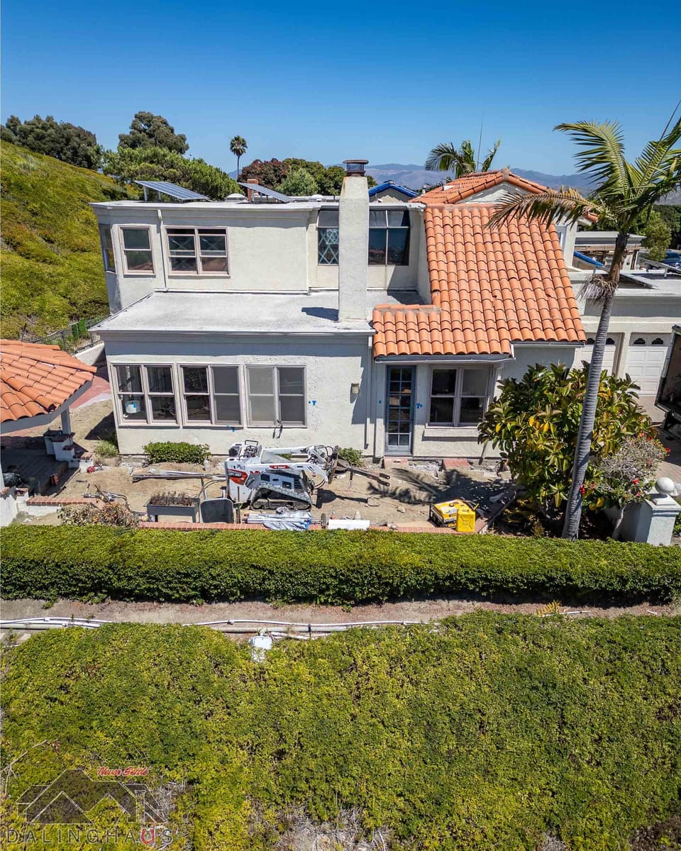 Two story home from the slope with a compact track loader and hydraulic drive head parked in the rear yard