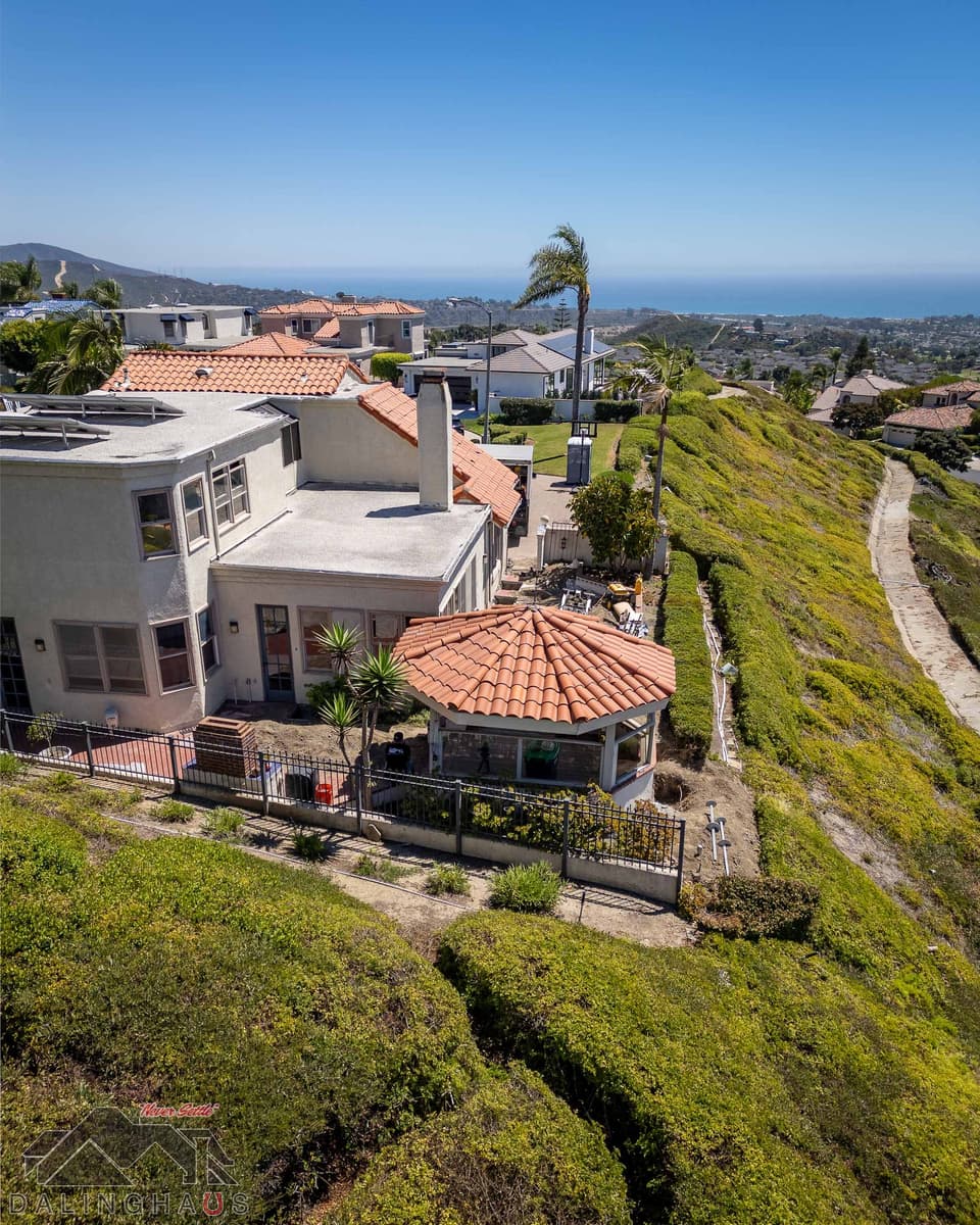 Rear corner of the home with a tile roofed sunroom, pier shafts staged on the slope and ocean beyond