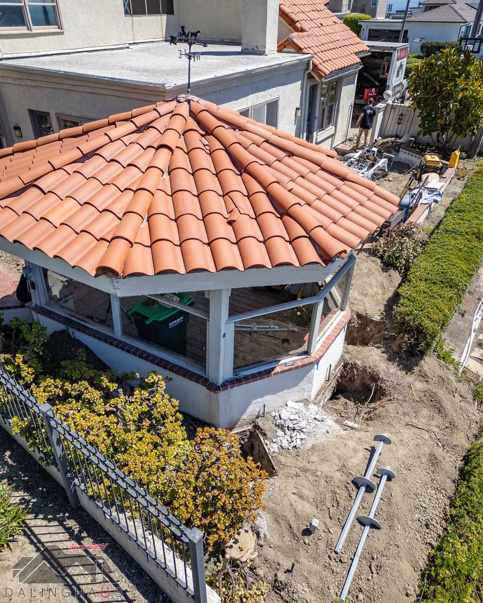 Close aerial of the sunroom with the footing exposed, broken concrete and helical pier sections laid on the dirt